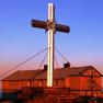 Großes Gipfelkreuz vor dem Alois-Günther-Haus bei Sonnenuntergang.