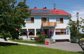 Ein zweistöckiges Gebäude mit der Aufschrift 'Gasthof Koller', umgeben von Bäumen und Rasen.