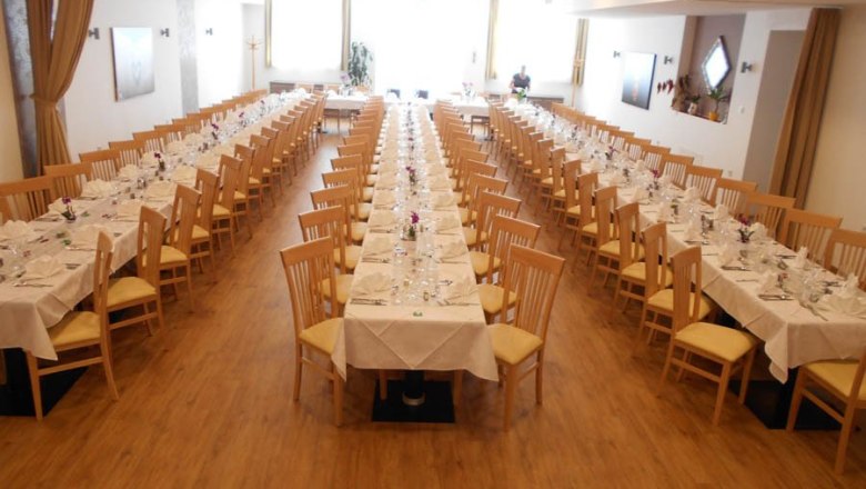 Großer, festlich gedeckter Saal mit drei langen Tischreihen und Holzstühlen.