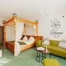 Ein gem&uuml;tliches Zimmer mit Himmelbett, gr&uuml;ner Couch und Wandtattoo.