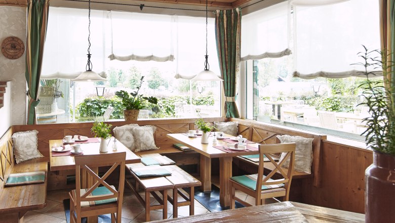Gemütlicher Frühstücksraum mit Holzmöbeln und großen Fenstern, die auf eine Terrasse blicken.