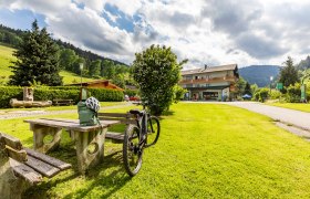 Ein Fahrrad steht neben einem Picknicktisch auf einer gr&uuml;nen Wiese vor einem Geb&auml;ude namens Hubertushof.