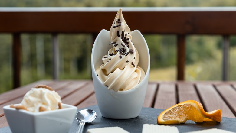 Ein Dessert mit Softeis, Schokostreuseln, Waffeln und Orangenscheibe auf einem Tisch.