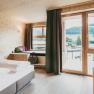 Modernes Hotelzimmer mit Holzw&auml;nden, gro&szlig;em Bett und Balkon mit Bergblick.