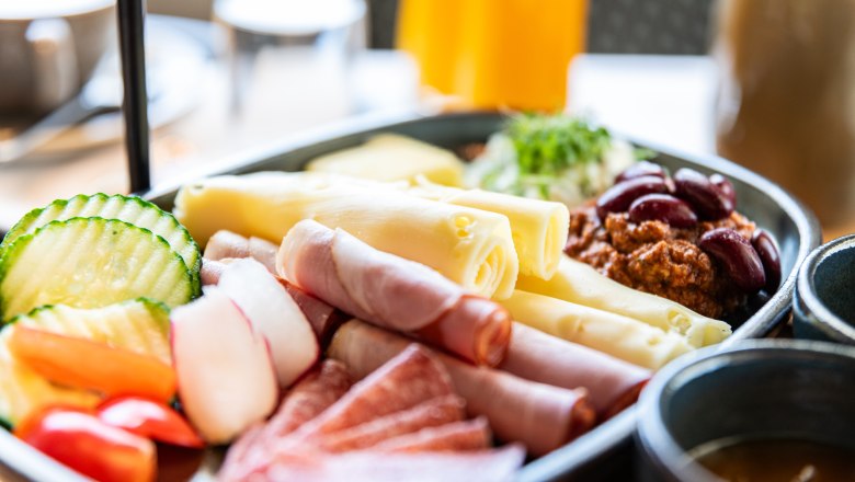 Nahaufnahme eines Frühstückstellers mit Käse, Schinken, Salami, Gemüse und Bohnen.