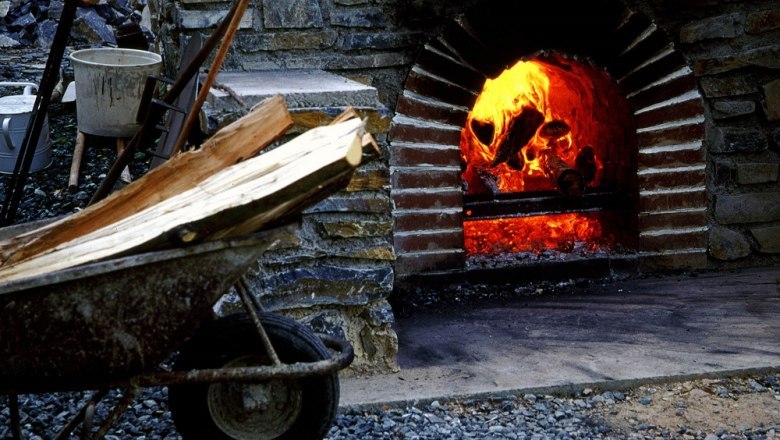 Ein brennender Kohlenmeiler mit Holzscheiten in einer Schubkarre davor.