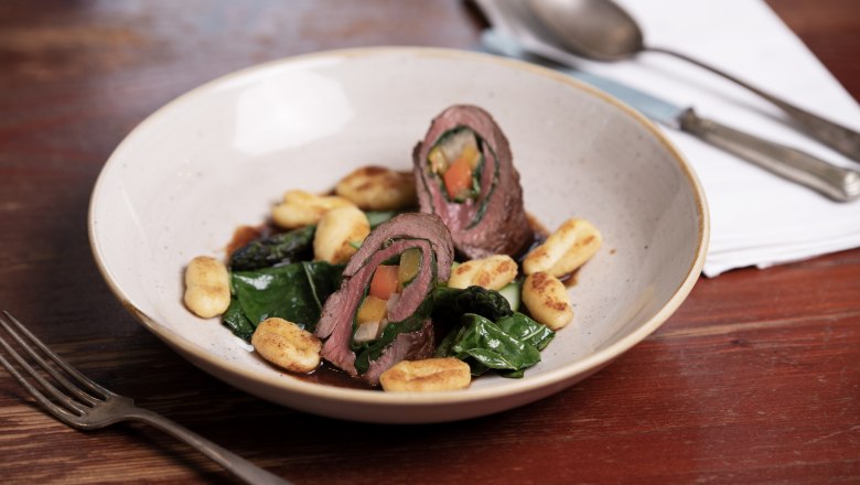 Roulade von der Rehschale mit Mangold und Wurzelgemüse, serviert mit Gnocchi auf einem Teller.