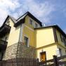 Gelbes Haus mit Holzdetails und Steinmauer, blauer Himmel im Hintergrund.