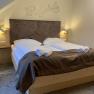 Ein gem&uuml;tliches Doppelzimmer mit gro&szlig;em Bett, dekoriert mit brauner Bettw&auml;sche und Handt&uuml;chern. An der Wand sind geometrische Muster.