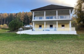 Zweist&ouml;ckiges Haus mit Balkon vor einem Wald.