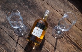 Eine Flasche Edelbrand mit zwei Gläsern auf einem Holztisch.