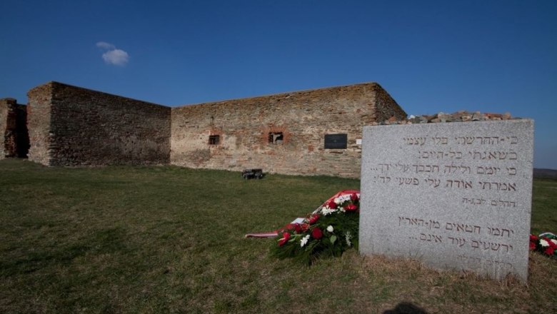 Gedenkstein mit hebr&auml;ischer Inschrift vor den Resten eines kreuzf&ouml;rmigen Steingeb&auml;ude.