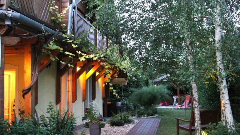 Gartenansicht eines Gästehauses mit beleuchteter Terrasse und Bäumen.