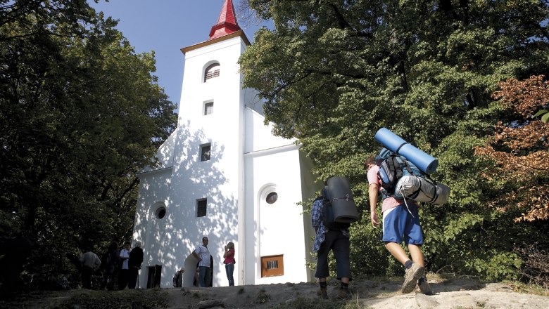 Wanderer mit Rucksack erreicht eine weiße Kirche im Wald.
