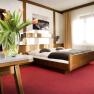 Ein gem&uuml;tliches Doppelzimmer mit einem Holzbett, roten Teppichboden und einem Tisch mit einem Blumenstrau&szlig; aus Tulpen.