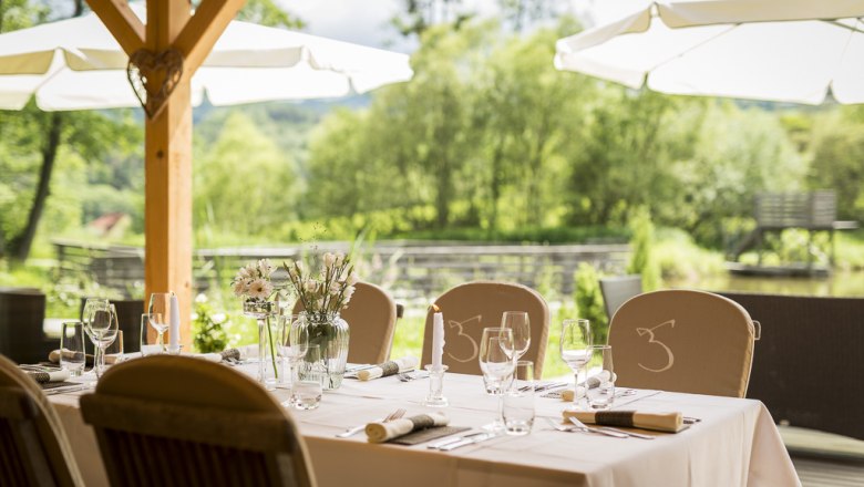 Gedeckter Tisch im Freien mit Blick auf einen Teich und Bäume.