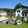 Ein l&auml;ndliches G&auml;stehaus mit Blumen und einem alten M&uuml;hlstein im Vordergrund.