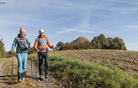 Zwei Wanderer auf einem Pfad in einer ländlichen Landschaft mit Hügel im Hintergrund.