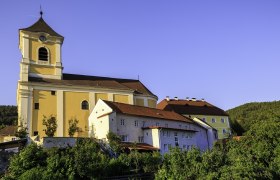 Pfarrkirche mit angrenzendem Kloster in sonniger Landschaft.