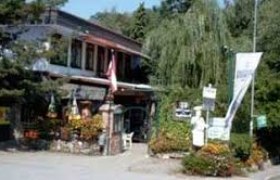 Ein eins&ouml;ckiges Geb&auml;ude mit Terrasse, umgeben von B&auml;umen und Pflanzen.