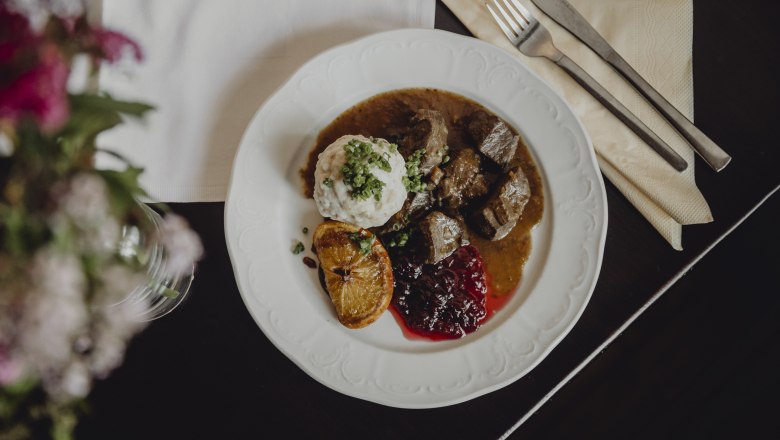 Ein Teller mit Hirschragout, Knödel, Preiselbeeren und einer gebratenen Zitronenscheibe.