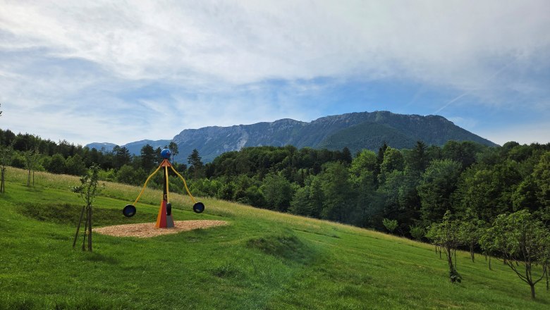 Ein Kinderspielplatz mit einer Wippe vor einer Berglandschaft mit der Rax im Hintergrund.