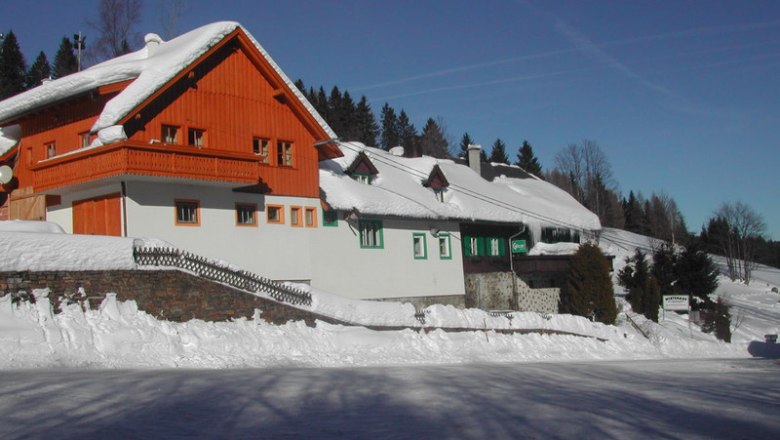 Verschneites Gasthaus mit Holzfassade und blauen Himmel im Hintergrund.