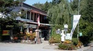 Ein eins&ouml;ckiges Geb&auml;ude mit Terrasse, umgeben von B&auml;umen und Pflanzen.