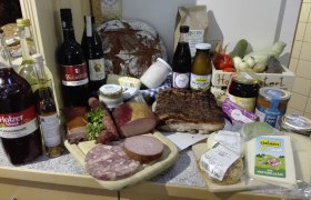 Verschiedene regionale Produkte wie Brot, Wurst, Käse und Getränke auf einem Tisch arrangiert.