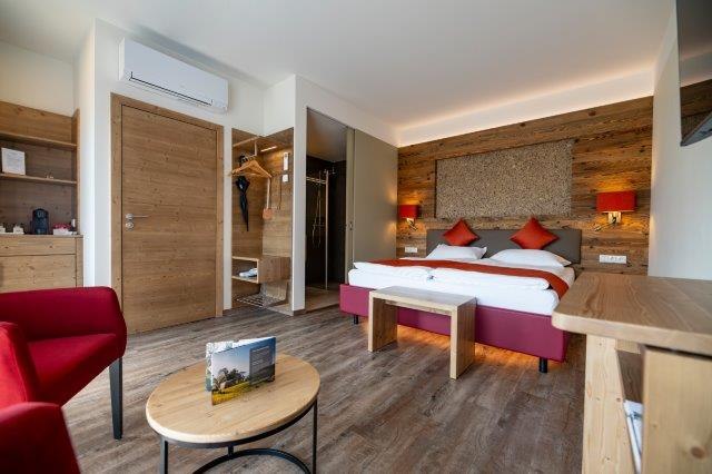 Modernes Gästezimmer mit Doppelbett, Holzmöbeln und roten Akzenten.