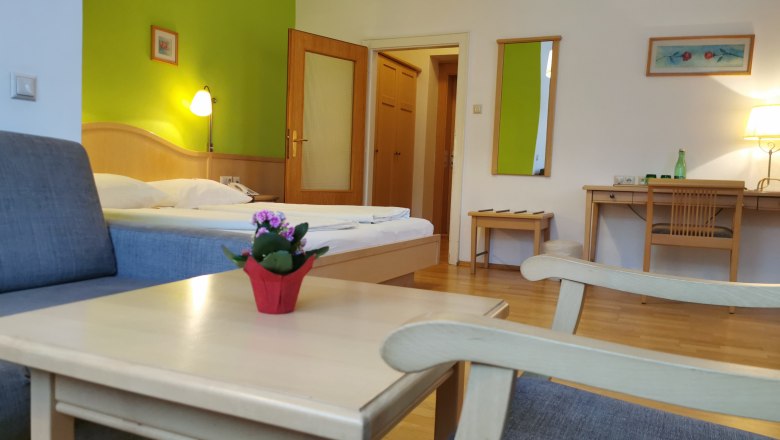 Hotelzimmer mit grünem Akzent, Bett, Schreibtisch und Sessel.