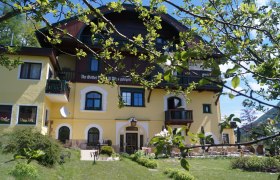 Gartenansicht des Hotel Belvedere mit gelber Fassade und bl&uuml;henden B&auml;umen im Vordergrund.
