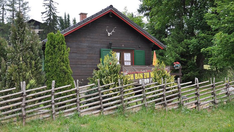 Weiglhütte a Semmeringen, © Weiglhütte Stefan Zimprich Egy rusztikus faház zöld redőnyökkel és fakerítéssel az előtérben, fákkal és bokrokkal körülvéve.