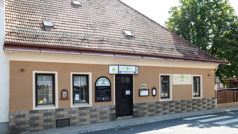 Historisches Gebäude mit brauner Fassade und Schildern. Es hat ein Ziegeldach und Fenster mit Gardinen.