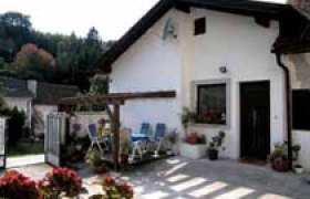 Ein kleines G&auml;stehaus mit Terrasse und Gartenm&ouml;beln vor einem wei&szlig;en Geb&auml;ude.