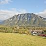 Panoramablick auf eine Berglandschaft mit Wiesen im Vordergrund und einem Dorf im Hintergrund.
