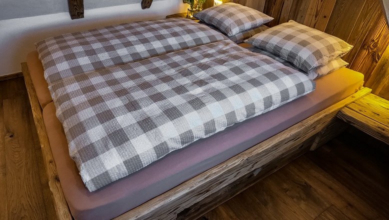 Gemütliches Bett mit kariertem Bettzeug in einer Holzhütte.