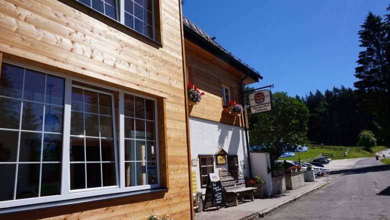 Holzfassade und Blumenk&auml;sten, sonniger Tag, Wald im Hintergrund.