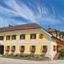 Traditionelles Gasthaus mit gelber Fassade, umgeben von gr&uuml;ner Landschaft und blauem Himmel.