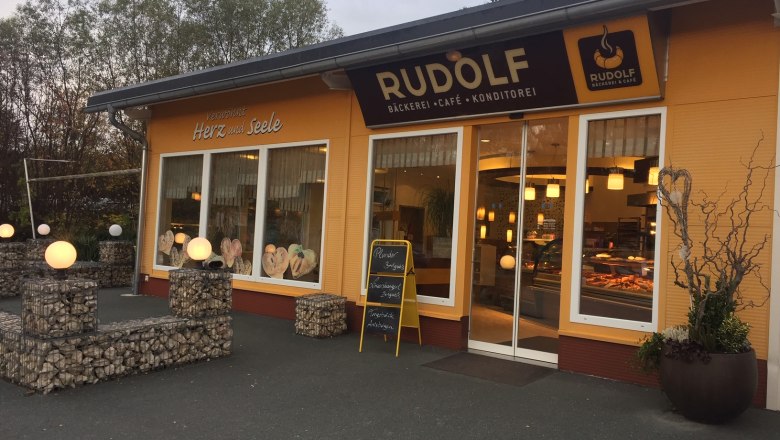 Außenansicht eines Cafés mit gelber Fassade und Schaufenstern.