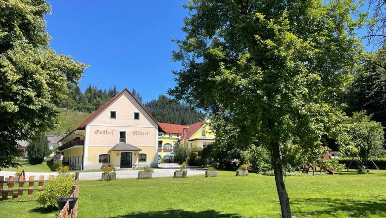 Ein traditioneller Gasthof mit gelber Fassade und rotem Dach in einer gr&uuml;nen Landschaft.