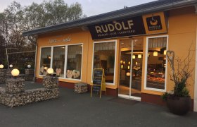 Außenansicht eines Cafés mit gelber Fassade und Schaufenstern.