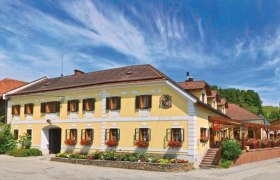 Traditionelles Gasthaus mit gelber Fassade, umgeben von gr&uuml;ner Landschaft und blauem Himmel.