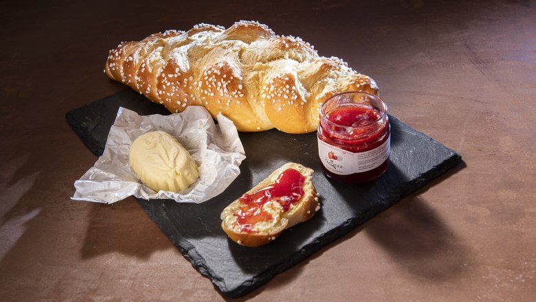 Ein Striezel mit Butter und Erdbeermarmelade auf einer Schieferplatte.