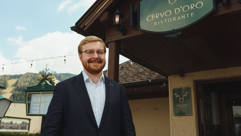 Ein Mann im Anzug steht lächelnd vor dem Restaurant Cervo D'Oro.