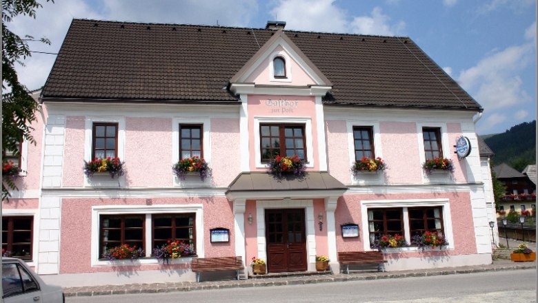 Gasthof Simml, © Familie Simml Ein traditionelles Gasthaus mit rosa Fassade und Blumenkästen an den Fenstern.