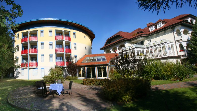 Zwei mehrstöckige Gebäude mit Garten und Tisch im Vordergrund.