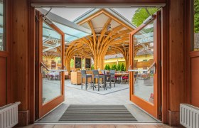 Offene Glast&uuml;ren f&uuml;hren zu einer Terrasse mit Holzdach und Sitzgelegenheiten.