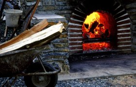 Ein brennender Kohlenmeiler mit Holzscheiten in einer Schubkarre davor.