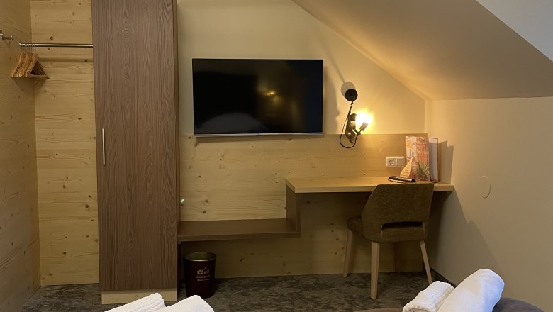 Ein gemütliches Hotelzimmer mit Doppelbett, Fernseher, Schreibtisch und Kleiderschrank.